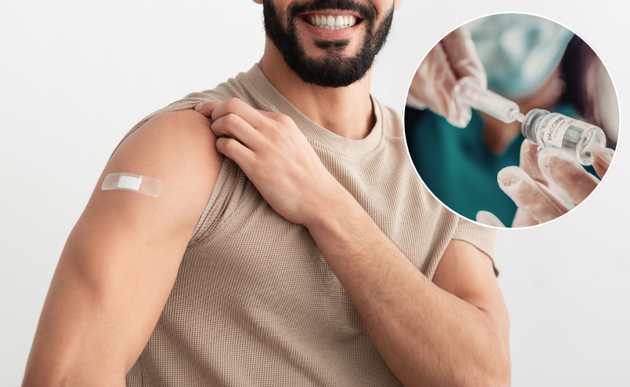 Closeup on the upper body and lower face of a man with light brown skin and a dark beard. He is smiling and wearing a tan coloured t-shirt, lifting up one sleeve to show a bandaid on his upper bicep. On the right of the image, a cutout shows a closeup of a needle drawing liquid from a vial labelled 'vaccination'.