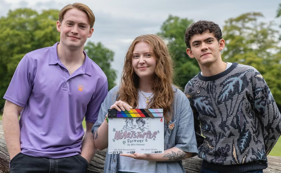Three people stand together, one holding a clapperboard that reads "Heartstopper forever".