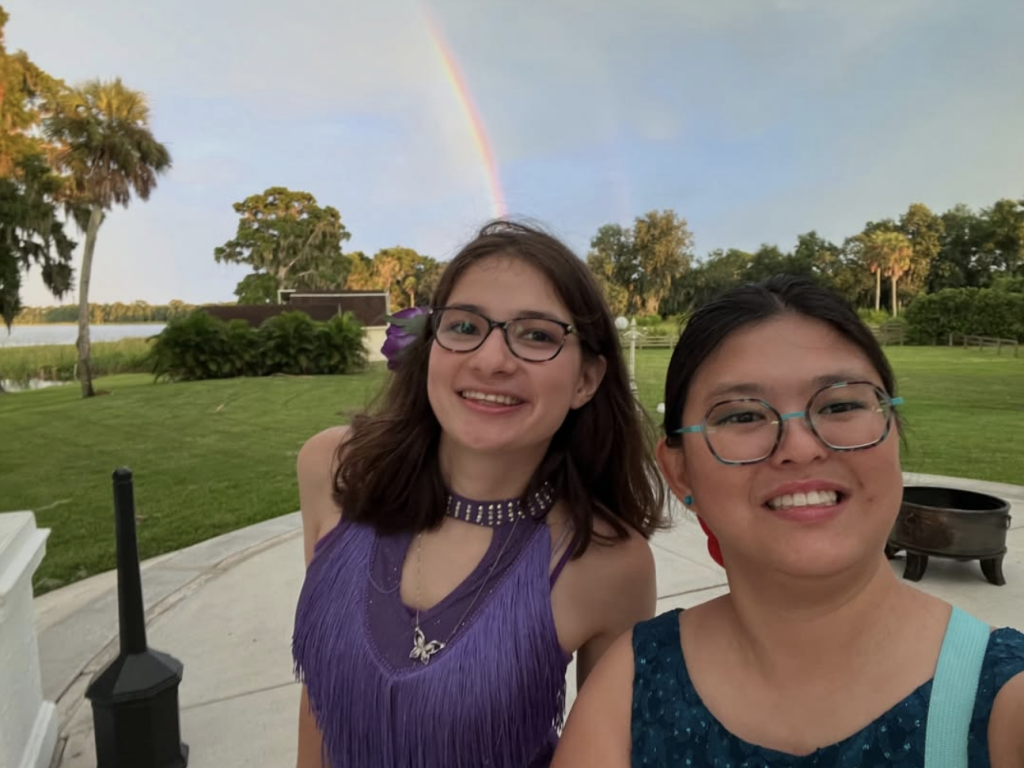 Pari and Tina standing together in front of a rainbow